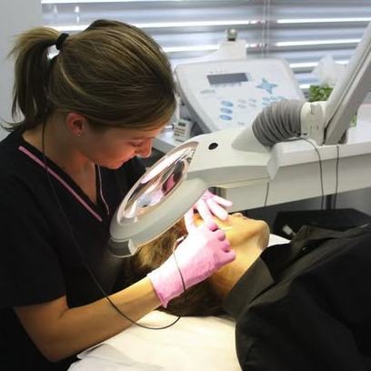 A licensed electrologist performing electrolysis under a magnifying lamp